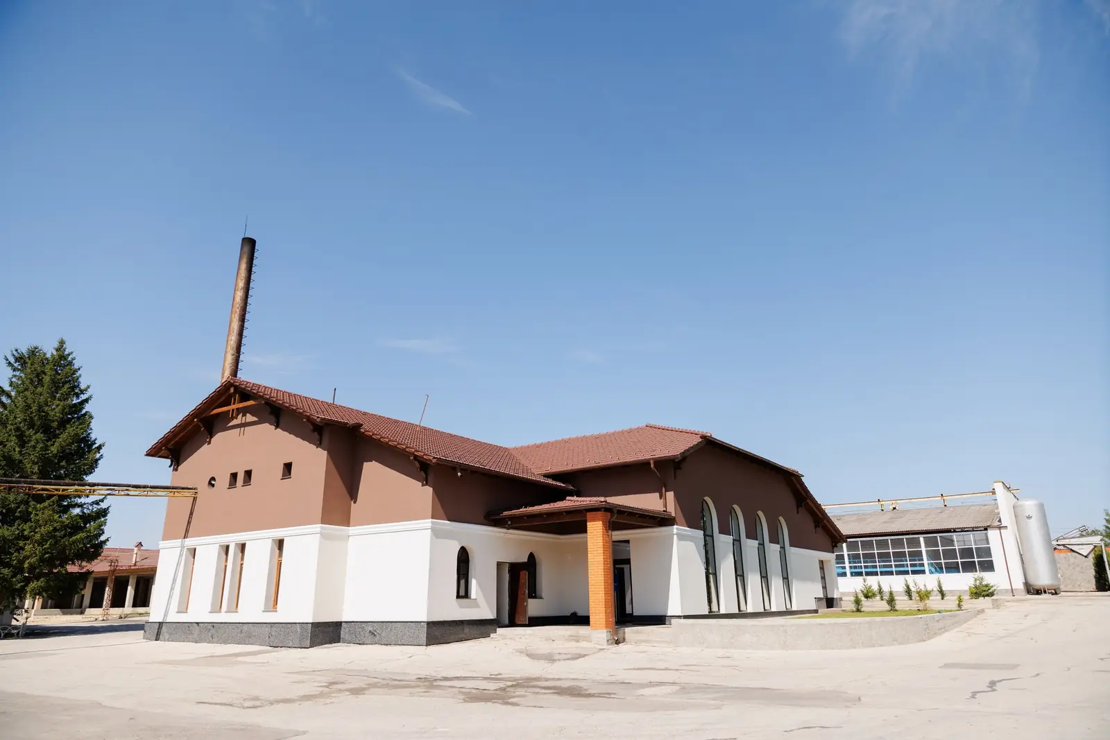 Clădirea principală a cramei de la Răzeni, cu acoperiș de țiglă și un coș înalt de cărămidă, sub cer senin