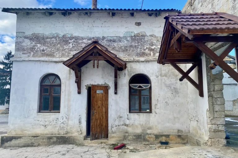 Intrarea unei clădiri vechi, văruite, cu streașini de lemn