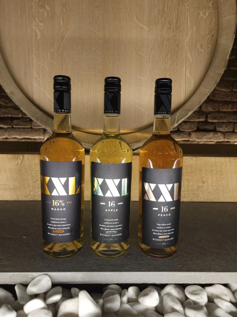 Trei sticle XXL, Mango, Apple și Peach, în fața unui butoi de stejar